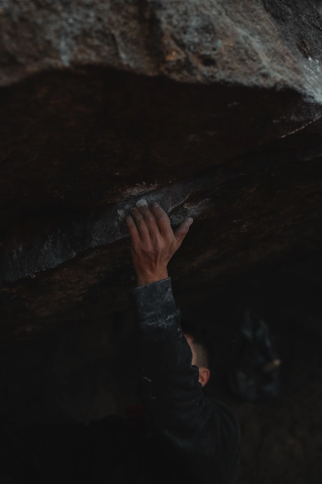 Chalked hand gripping a dark rock hold during a session