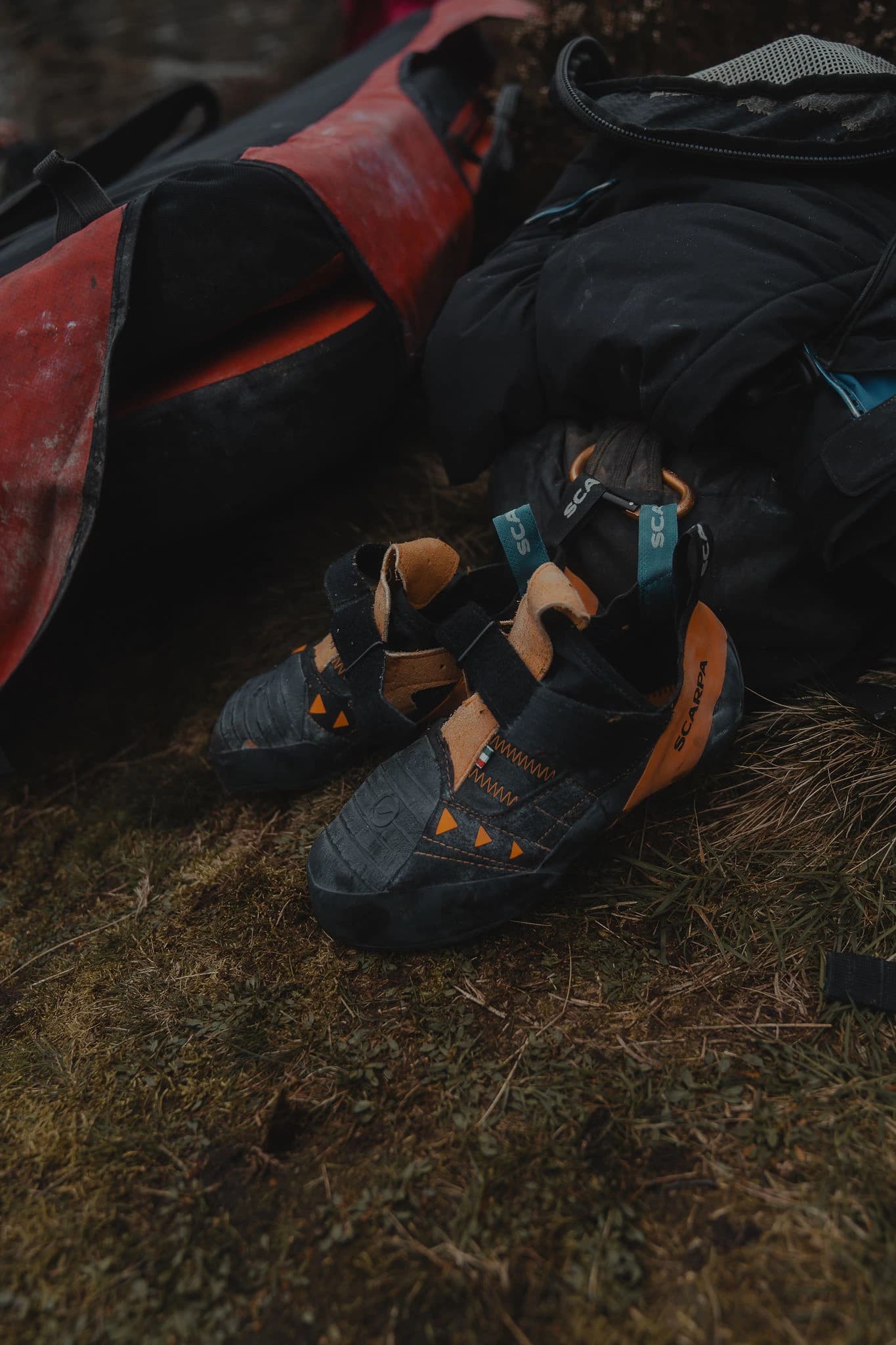 Worn climbing shoes resting beside a crash pad and kit bag outdoors